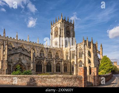 Une église du XIIe siècle attrapée par la lumière du soleil du soir. Il est entouré par un mur de briques avec une porte en bois et un ciel avec des nuages est au-dessus. Banque D'Images