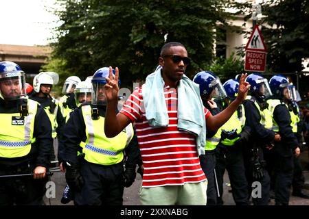 Londres, Royaume-Uni, 25 août 2024. L'homme montre un signe de paix devant la ligne de police anti-émeute après l'arrestation de 3 hommes. Crédit : Martin Suker/Alamy Live News Banque D'Images