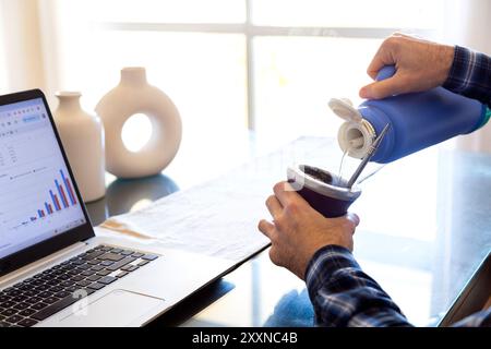 Homme travaillant et buvant yerba mate. Préparation d'un partenaire avec de l'eau chaude. Gourd mate avec yerba à l'intérieur. Homme latino-américain d'âge moyen travaillant avec un ordinateur portable Banque D'Images