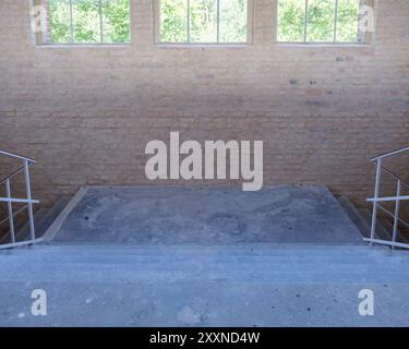 La lumière vive des fenêtres suspendues illumine un palier d'escalier brut et sale dans une installation industrielle. Banque D'Images