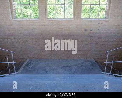 La lumière vive des fenêtres suspendues illumine un palier d'escalier brut et sale dans une installation industrielle. Banque D'Images