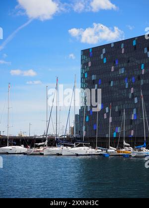 Reykjavik, Islande - 9 mai 2024 : une scène portuaire moderne avec des yachts élégants amarrés près d'un bâtiment frappant aux motifs géométriques colorés, Under Banque D'Images