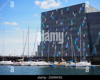 Reykjavik, Islande - 9 mai 2024 : une scène portuaire moderne avec des yachts élégants amarrés près d'un bâtiment frappant aux motifs géométriques colorés, Under Banque D'Images