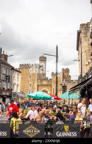 Les gens appréciant le temps chaud manger et boire dehors le long de High Street dans la capitale galloise de Cardiff avec une vue sur le château de Cardiff Banque D'Images