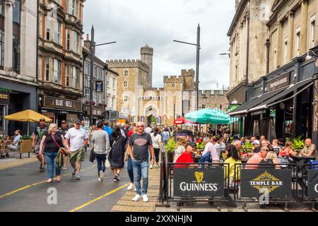 Les gens appréciant le temps chaud manger et boire dehors le long de High Street dans la capitale galloise de Cardiff avec une vue sur le château de Cardiff Banque D'Images