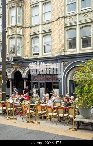 Les gens appréciant le temps chaud manger et boire dehors le long de High Street dans la capitale galloise de Cardiff avec une vue sur le château de Cardiff Banque D'Images