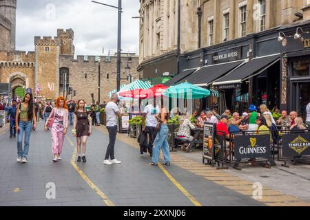 Les gens appréciant le temps chaud manger et boire dehors le long de High Street dans la capitale galloise de Cardiff avec une vue sur le château de Cardiff Banque D'Images