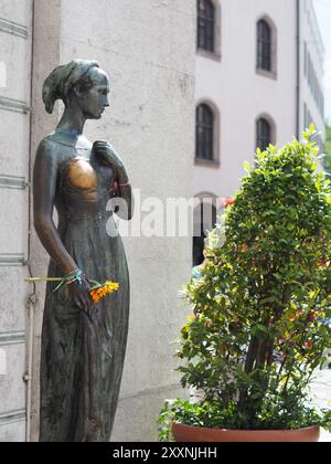 Munich, Allemagne - 3 août 2024 : cette image représente une statue en bronze d'une femme tenant des fleurs, située sur une place publique, évoquant un sentiment de beauté Banque D'Images