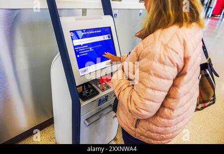 Jeune femme s'enregistrant dans un aéroport à l'aide d'un kiosque libre-service. New York. ÉTATS-UNIS. Banque D'Images