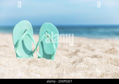 Tongs turquoise ou bleu clair ou chaussures de sable collées dans le sable sur la plage de sable au bord de la mer ou de l'océan. Concept de voyage ou de vacances dans Hot co Banque D'Images