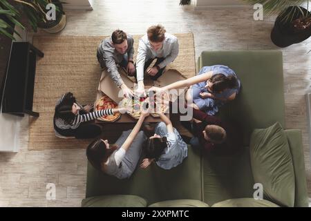 Une fête de pizza, un groupe d'amis discutant et mangeant joyeusement de la pizza à la table et buvant de l'eau gazeuse sucrée. Vue de dessus depuis le deuxième étage. Banque D'Images