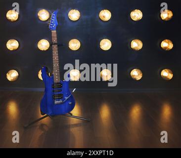 Music concept. Guitare électrique bleu debout sur le plancher en bois près du mur sous les feux de croisement Banque D'Images