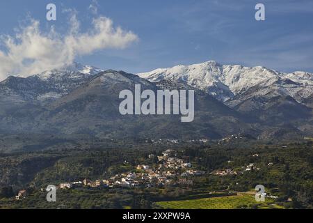 Petit village dans le paysage vallonné sous les montagnes enneigées et le ciel bleu, vignoble, oliveraies, Lefka Ori, montagnes blanches, massif montagneux, Ouest, Banque D'Images