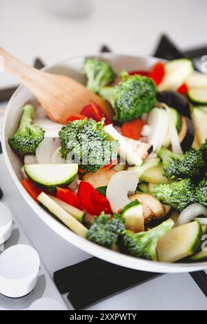 Au-dessus des tranches de brocoli frais de tomates de squash et d'aubergine dans une poêle avec spatule en bois sur cuisinière Banque D'Images