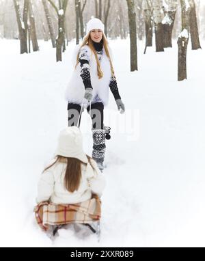 Petite fille s'amusant sur un traîneau dans la neige avec sa mère Banque D'Images