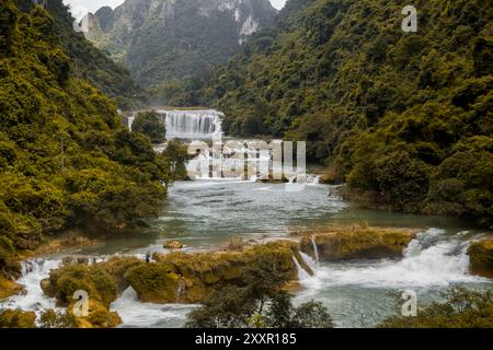 Une série de cascades coulent à travers une vallée luxuriante et boisée entourée de collines verdoyantes, créant une scène naturelle pittoresque et sereine Banque D'Images