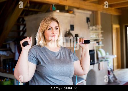 Femme en surpoids exerçant à la maison, tenant la corde à sauter. Entraînement à la corde à sauter dans le salon. Banque D'Images