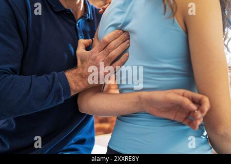 Gros plan des mains d'un ostéopathe traitant l'épaule d'un patient lors d'une séance de thérapie manuelle professionnelle. Met en valeur les techniques de manipulation douce Banque D'Images