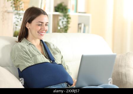 Femme convalescente heureuse utilisant un ordinateur portable assis sur un canapé à la maison Banque D'Images