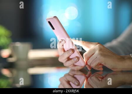 Gros plan d'une main de femme utilisant un téléphone rose dans la nuit à la maison Banque D'Images