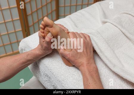 Gros plan d'un massage relaxant des pieds dans un spa. Les mains pressent doucement la semelle, favorisant le bien-être, le soulagement du stress et la relaxation thérapeutique. Banque D'Images