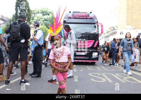 Londres, Royaume-Uni, 25 août 2024. Carnaval annuel des enfants le dimanche jour férié. Des centaines de milliers de personnes viennent à Notting Hill pour célébrer la nourriture, les boissons et la culture des Caraïbes pleines de couleurs et de costumes colorés. En image, une jeune fille des Caraïbes sourit devant le défilé portant une tenue rose carnavale des Caraïbes et une robe de tête à plumes. Crédit : Martin Suker/Alamy Live News Banque D'Images