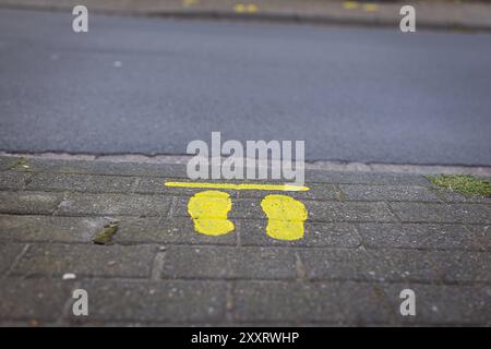 Melle, Deutschland 29. Novembre 2022 : Themenbild - Symbolbilder - Sicherer Schulweg - 2024 Im Bild : auf einem Gehweg an einer Verkehrsstraße sind gelbe Füße angebracht. Die gelben Markierungen zeigen den Schulanfängern an, WO eine gefahrenreduzierte Querungsstelle über die Straße führt. Landkreis Osnabrück Niedersachsen *** Melle, Allemagne 29 novembre 2022 image thématique images symboliques itinéraire sûr vers l'école 2024 dans l'image des pieds jaunes ont été placés sur un trottoir le long d'une route les marques jaunes indiquent aux enfants qui commencent l'école où un point de passage à danger réduit mène à travers la route Banque D'Images