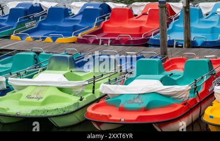 Seebruck am Chiemsee, Allemagne. 26 août 2024. Des pédalos colorés se trouvent à proximité sur une jetée sur la rive du lac Chiemsee. Le lac Chiemsee, également connu sous le nom de mer de Bavière, est le plus grand lac de Bavière et le troisième plus grand lac d'Allemagne après le lac de Constance et le lac Müritz. Crédit : Peter Kneffel/dpa/Alamy Live News Banque D'Images