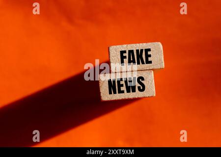 Faux message écrit sur des blocs de bois avec fond orange. Symbole conceptuel de fausses nouvelles. Copier l'espace. Banque D'Images