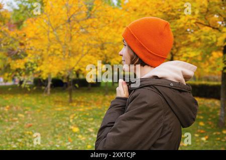 Femme vue de côté portant bonnet et veste chaude se tient dans le parc d'automne avec un feuillage d'automne vibrant Banque D'Images