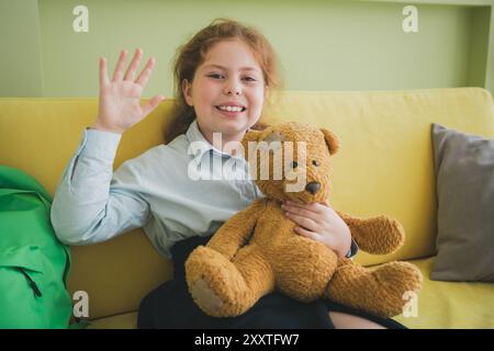 Photo de bonne humeur mignonne petite fille assise canapé agitant bras confortable appartement de chambre à l'intérieur Banque D'Images