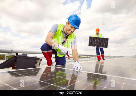 Équipe de travailleurs sur le toit d'un bâtiment travaillant à la réparation de panneaux solaires. Banque D'Images