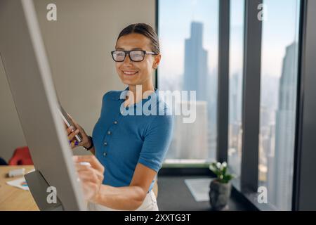 Une femme professionnelle activement engagée dans son travail à l'intérieur d'un bureau moderne avec une vue sur la ville Banque D'Images