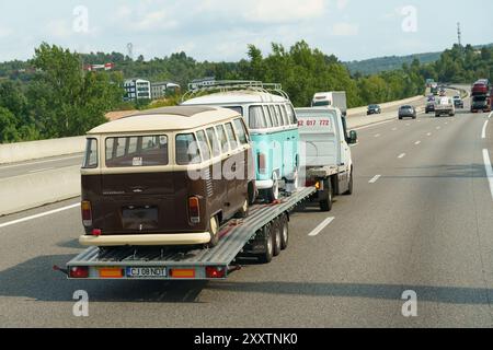 Nice, France - 6 juin 2023 : deux fourgonnettes Volkswagen d'époque sont remorquées sur une remorque à plateau sur une autoroute entourée d'arbres verts et d'un espace dégagé Banque D'Images