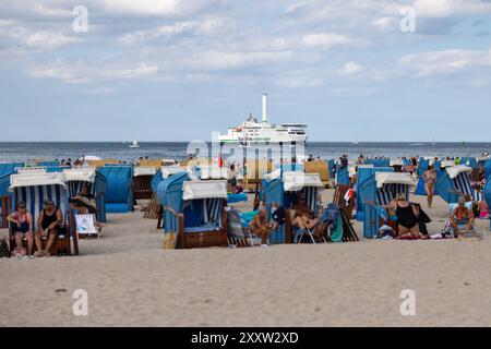 Strand von Warnemünde an der Ostsee Sommer 2024 Warnemuende, Deutschland 24. Août 2024 : eine Fähre passiert die Ostsee während Menschen einen heißen Sommertag BEI 30 Grad Celsius am Strand von Warnemünde an der Ostsee in Deutschland im Sommer 2024 genießen. Mecklembourg-Poméranie occidentale Banque D'Images