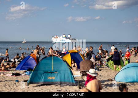 Strand von Warnemünde an der Ostsee Sommer 2024 Warnemuende, Deutschland 24. Août 2024 : eine Fähre passiert die Ostsee während Menschen einen heißen Sommertag BEI 30 Grad Celsius am Strand von Warnemünde an der Ostsee in Deutschland im Sommer 2024 genießen. Mecklembourg-Poméranie occidentale Banque D'Images