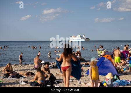 Strand von Warnemünde an der Ostsee Sommer 2024 Warnemuende, Deutschland 24. Août 2024 : eine Fähre passiert die Ostsee während Menschen einen heißen Sommertag BEI 30 Grad Celsius am Strand von Warnemünde an der Ostsee in Deutschland im Sommer 2024 genießen. Mecklembourg-Poméranie occidentale Banque D'Images