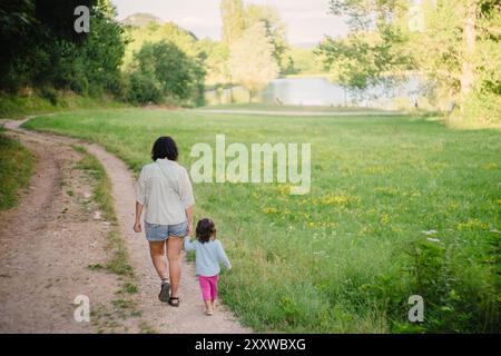 Mère et fille marchant ensemble le long du chemin dans la nature main dans la main. Concept de grandir ensemble dans l'enfance Banque D'Images