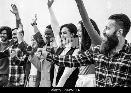 Groupe de jeunes adultes divers célébrant avec les poings levés et de larges sourires dans une photo en noir et blanc. L’image capture un moment d’unité et de partage Banque D'Images