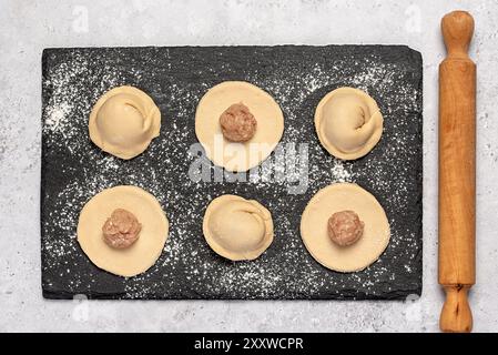 Photographie macro-alimentaire des ingrédients de boulettes maison, pâte crue et poulet haché, oignon, ravioli, tortellini, rouleau à pâtisserie Banque D'Images