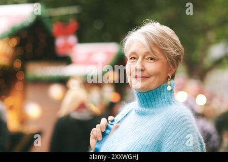 Portrait en gros plan extérieur de belle et heureuse femme de 55 à 60 ans visitant le marché de Noël Banque D'Images