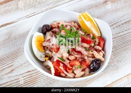 Piyaz, salade de haricots blancs turcs avec tomates, oignon rouge et persil, assaisonnée de sumac et vinaigrette à l'huile d'olive, dans une assiette en céramique blanche sur un bois Banque D'Images