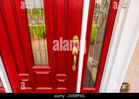 Gros plan d'une porte d'entrée en chêne rouge avec inserts en verre présentant des motifs floraux, une serrure dorée et une poignée. Banque D'Images