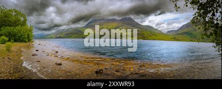 Les eaux scintillantes du Loch Maree reflètent les imposantes montagnes vertes, tandis que les nuages sombres planent au-dessus, créant une atmosphère captivante. Banque D'Images