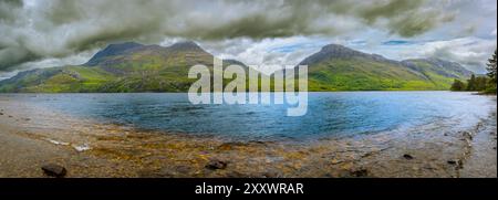 Les eaux scintillantes du Loch Maree reflètent les imposantes montagnes vertes, tandis que les nuages sombres planent au-dessus, créant une atmosphère captivante. Banque D'Images