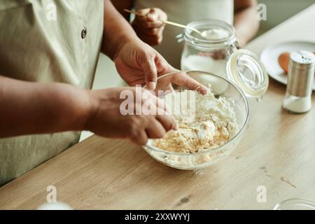 Gros plan sur les mains de la femme noire senior remuant la levure chimique et les œufs dans un bol en verre pour faire cuire des crêpes avec sa petite-fille sur le comptoir de cuisine en bois, espace de copie Banque D'Images