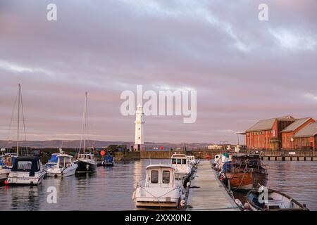 ÉDIMBOURG - 13 JANVIER 2024 : coucher de soleil serein sur le port de Newhaven, mettant en évidence le phare et les bateaux amarrés. Banque D'Images