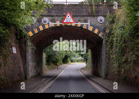 Pont de chemin de fer en briques basses traversant une route étroite avec un panneau de restriction de hauteur, un jour d'été tranquille Banque D'Images