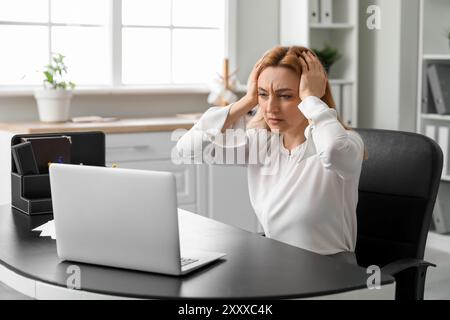 Femme adulte souffrant de maux de tête avec ordinateur portable au bureau Banque D'Images