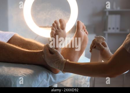 Esthéticienne pulvérisant un produit cosmétique sur les pieds de l'homme dans le salon de spa, gros plan Banque D'Images